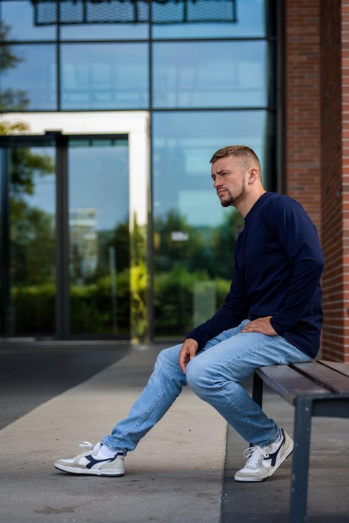 Mężczyzna siedzący na ławce w granatowym longsleevie.